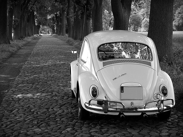 A volkswagen Beetle parked on a countryside road in black and white